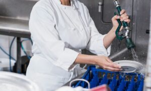 restaurant worker washing dishes with hot water thanks to Houston commercial plumber
